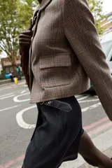 Blazer corto de corte estructurado con cuello solapa, manga larga y hombreras. Presenta cierre frontal con botones metálicos y dos bolsillos delanteros de plastrón con solapa. Diseño con estampado de cuadros tipo príncipe de gales.