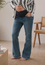 Jeans de maternidad corte flare en denim azul, con faja elástica de altura media para la panza y dobladillo desflecado en las pantorrillas.