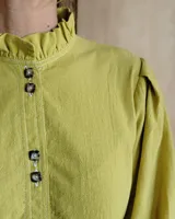 Camisa de manga tres cuartos color beige con cuello con volados y botones frontales. Presenta un detalle de color negro en la parte superior de las mangas.