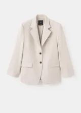 Blazer color beige con solapas de muesca, cierre frontal de dos botones oscuros, bolsillos con solapa en los laterales y un bolsillo ojal en el pecho.