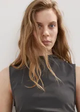 Vestido corto color gris oscuro, sin mangas y con cuello alto. Presenta un diseño entallado con panel fruncido en la cintura y falda asimétrica con volados.
