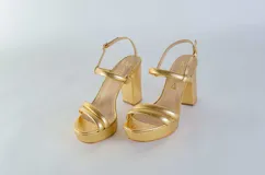 Sandalia de cuero con plataforma y taco cuadrado alto. Presenta una tira delgada en el tobillo con cierre de hebilla metálica y dos tiras acolchadas en la parte frontal.