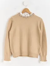 Sweater de punto color beige, con cuello redondo adornado con apliques de pedrería y detalle de puntilla blanca en el cuello y los puños.