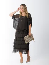 Vestido midi de seda italiana color negro, diseño dos en uno con capa superior de calce amplio, falda con volados y forro interior de algodón elastizado.