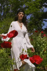 Vestido blanco de crepe con escote en V, mangas largas abullonadas con elástico en los puños, largo irregular, lazo para ajustar en la cintura y volado en el ruedo.