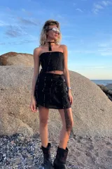 Conjunto de dos piezas compuesto por un top strapless y una falda corta tipo pareo, confeccionados en una combinación de lino y tul con bordado de pequeñas perlas metálicas en tono oro viejo.