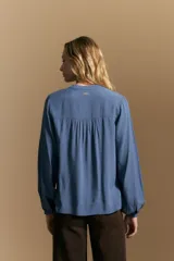 Camisa de manga larga color blanco, con cuello mao y escote en V. Presenta frunces en el canesú, cierre frontal con botones y mangas amplias con puños abotonados.