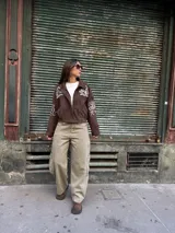 Campera tipo bomber color chocolate, confeccionada en gamuza, con cierre frontal y bordados en color natural con diseño de arabescos en el pecho y las mangas.