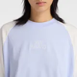 Remera New Balance de algodón con diseño de mangas raglán en color blanco y cuerpo en color lila. Presenta cuello redondo y un gráfico bordado con el nombre de la marca en el centro del pecho.
