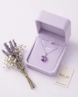 Collar de plata con cadena fina y dije en forma de corazón de cristal violeta tornasolado. Incluye aros haciendo juego con el mismo diseño de corazón.