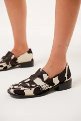 Mocasín de cuero con pelo y estampado de vaca en blanco y negro. Presenta horma cuadrada, diseño enrejillado en la capellada y taco bajo de 4,5 cm.