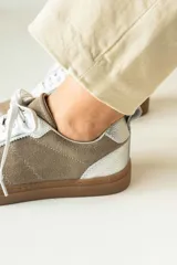 Championes urbanos de gamuza color marrón, con detalles en charol negro y bordes dorados. Presentan cordones negros y suela de goma al tono.