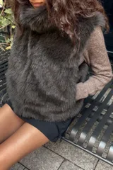 Chaleco de pelo sintético color verde oscuro, con cuello alto y sin mangas. Cierre frontal con ganchos metálicos forrados.