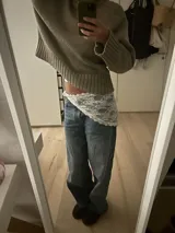 Pañuelo de encaje blanco con diseño floral, de forma triangular, ideal para usar como accesorio sobre la cintura o como detalle decorativo en la vestimenta.