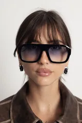 Lentes de sol con armazón de policarbonato negro y diseño de puente alto. Presentan cristales con degradado en tonos azulados y protección UV400.