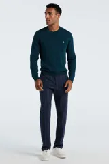 Sweater de punto color verde oscuro, con cuello redondo, mangas largas y puños acanalados. Presenta un pequeño logo bordado en el pecho.