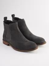 Bota Chelsea de gamuza gris con elásticos laterales, suela de goma marrón y tirador trasero.