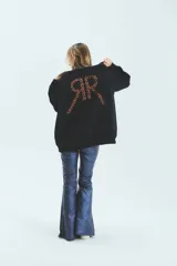 Buzo negro oversize de frisa esmerilada con cuello alto, hombros caídos, bolsillos laterales y estampa en la espalda con el logo de la marca en animal print.