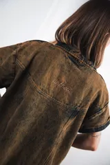 Vestido corto marrón con efecto desgastado, cuello camisero, cierre frontal con cremallera metálica, mangas cortas, dos bolsillos frontales y bordados de soles en el canesú delantero y trasero.