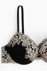 Soutien push-up con aros, copas acolchadas y breteles ajustables. El cuerpo es negro, con cobertura de encaje floral en color beige claro en la parte superior de las copas y en el contorno.