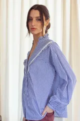 Camisa a rayas verticales rojas y blancas con cuello mao y mangas 3/4 abullonadas. Presenta detalles de puntilla blanca en el canesú. Cierre frontal con botones.