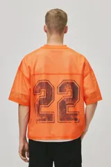 Remera de malla color naranja vibrante, estilo jersey de fútbol americano, con cuello en V y corte oversized. Presenta un estampado grande y desgastado del número "22" en color negro o marrón oscuro en el frente.