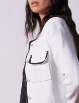 Chaqueta de tweed negra marca Nanette, con escote a la base, abertura central con botones, bolsillos delanteros, aplique de botones perlados en los puños, ribete en contraste blanco y forro interno.