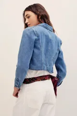 Saco corto de denim azul con solapas y bolsillos ribeteados, confeccionado en mezcla de algodón y poliéster.