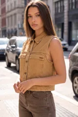 Chaleco de denim color camel con efecto lavado, cuello camisero, cierre frontal con botones metálicos y dos bolsillos frontales con solapa.