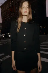 Chaqueta de punto color negro con cuello redondo, manga por debajo del codo con hombros marcados y acabados en rib. Cierre frontal con botones dorados.