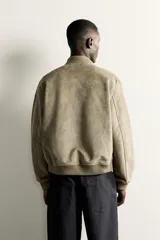Campera bomber color verde militar de corte relaxed fit, confeccionada en tejido efecto ante, con cuello, puños y dobladillo en rib elástico, bolsillos frontales de vivo y cierre central con cremallera.