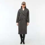 Abrigo largo de mujer, estilo lanoso, con estampado de pata de gallo o príncipe de Gales en tonos grises y marrones. Presenta un corte recto y holgado, cuello con solapas anchas y cierre cruzado con doble botonadura oscura.