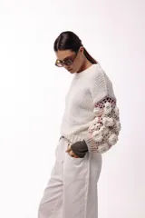 Sweater de punto con cuerpo liso en color negro y mangas largas tejidas en crochet gris con aplicaciones de flores en relieve color blanco.