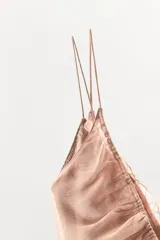 Vestido corto de satén con escote en pico y tirantes finos. Presenta un diseño con superposición de capas, detalle de lazada frontal y aplicaciones de encaje a tono en el cuerpo y el bajo con terminación en ondas.