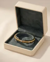 Pulsera tipo esclava rígida de acero con baño de oro, con diseño estriado y detalles de incrustaciones de circonia.