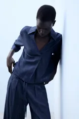 Camisa de lino azul, con cuello solapa, escote en V y mangas por debajo del codo.