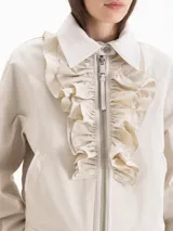 Campera bomber color beige, confeccionada en una mezcla de poliéster y algodón, con cuello camisero, cierre frontal con cremallera y volados superpuestos en la pechera.