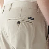 Pantalón chino color beige, de corte recto, con bolsillos laterales y traseros. Se ajusta a la cintura con cinturón de cuero marrón.