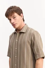 Camisa de manga corta oversize color beige, con diseño de rayas verticales blancas, cuello clásico y cierre frontal de botones.