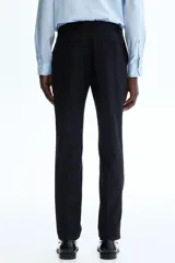 Pantalón de traje negro de corte slim fit, con bolsillos laterales, bolsillos traseros ribeteados y raya marcada en las perneras. Cuenta con cierre de cremallera y corchete oculto.
