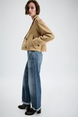 Trench corto cruzado de piel de ante color tostado, con cuello de solapa, bolsillos delanteros de vivo y manga larga con trabillas en los puños.