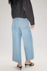 Jeans de tiro alto con pernera ancha y corte cropped. Presenta diseño de cinco bolsillos, cierre frontal con cremallera y botón, e incluye un cinturón de gamuza marrón con hebilla metálica.