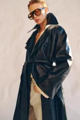 Trench oversize de efecto piel color azul marino, con cuello solapa, manga larga, bolsillos delanteros y cinturón ajustable del mismo tejido. Cierre frontal cruzado con botones y forro interior.