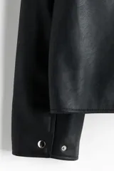 Campera de cuero sintético color negro con cuello camisero, cierre frontal, bolsillo superior con cierre y bolsillos laterales ribeteados.
