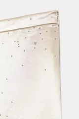 Pantalón de tiro alto y pernera ancha, confeccionado en tejido satinado con aplicación de brillos distribuidos por toda la prenda. Cuenta con cierre lateral mediante cremallera oculta.