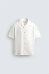 Camisa de corte relajado confeccionada en popelín de algodón, con cuello bowling y manga corta. Presenta cierre frontal de botones y bajo con aberturas laterales.