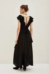 Vestido largo negro con escote en V y volados en el borde del escote y mangas. Presenta un corte peplum con elástico en la cintura y falda larga con abertura frontal y volados.