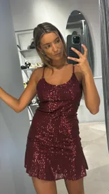 Vestido corto de fiesta color bordó, confeccionado en tela con lentejuelas. Presenta breteles finos, escote redondo y un diseño con volado en el ruedo.