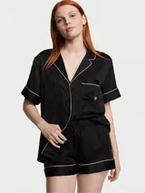 Pijama corto de satén negro con estampado monograma sutil, ribetes blancos y diseño de botones frontales.
