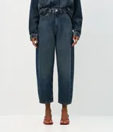 Pantalón de jean modelo carrot con cintura alta, corte holgado en caderas y piernas que se estrechan hacia el tobillo. Confeccionado en denim de algodón con lavado medio, cuenta con cinco bolsillos funcionales, cierre frontal con botón y cremallera, y trabillas para cinturón.